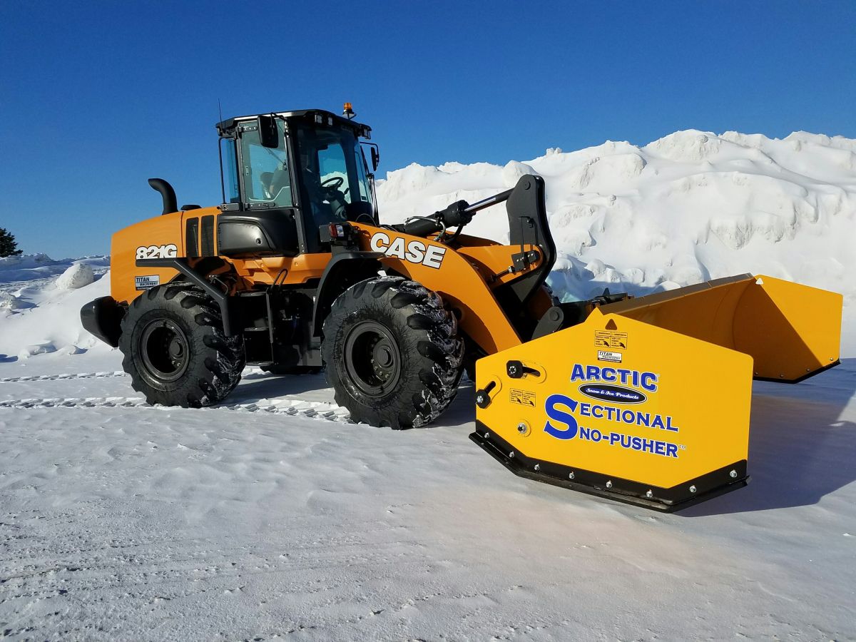 A heavy-duty CASE front-end loader equipped with an Arctic snow plow attachment actively clearing a massive commercial parking lot