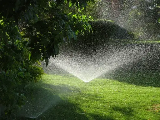 A green lawn sprinkler head in dynamic action, spraying pristine water droplets in a wide arc against a dark background